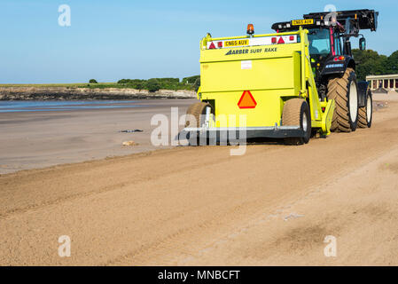 Whitmore Bay Beach bei Barry Island, Wales, früh an einem hellen, sonnigen Sommermorgen der Wurf durch einen roten Traktor ziehen einer Friseur Surfen Rechen gesäubert werden. Stockfoto