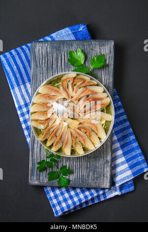 Marinierter Hering in Öl auf einem Holzbrett auf einem grauen dunklen Tisch. Snack Stockfoto