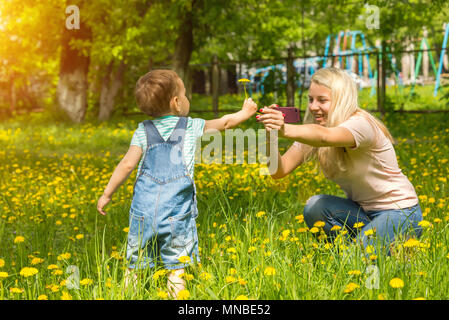 Mama nimmt Bilder des Kindes am Telefon, in einer grünen Wiese auf dem Gras Stockfoto
