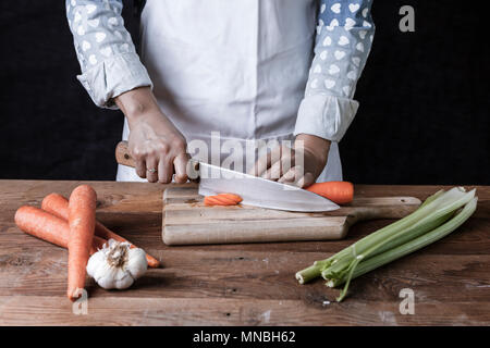 Schneiden Möhren auf einem Schneidebrett mit Sellerie und Knoblauch auf dem Tisch. Stockfoto