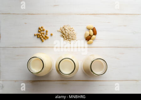 Overhead shot von Soja, Hafer und Mandelmilch Getränke in einer Reihe von offenen Flaschen mit Zutaten aus weiß lackiert, Holz beplankt. Geringe Tiefe von fie Stockfoto