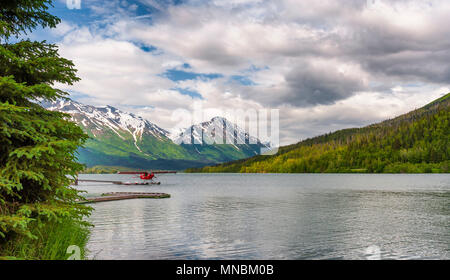 Ein Wasserflugzeug auf Moose Lake in Alaska, mit der Chugach Berge im Hintergrund bei bewölktem Himmel. Stockfoto