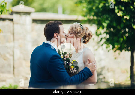 Glücklich lächelnde stilvolle Braut und Bräutigam im Sommer, grünen Park mit Blumenstrauß, Tanzen und Spaß am Tag ihrer Hochzeit Stockfoto