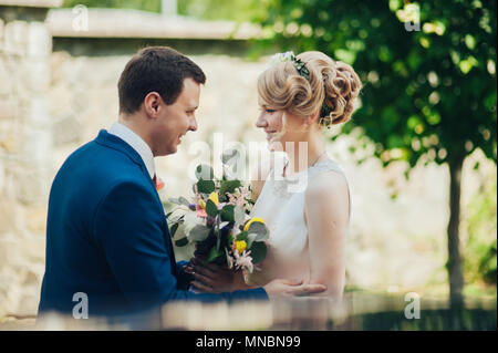 Glücklich lächelnde stilvolle Braut und Bräutigam im Sommer, grünen Park mit Blumenstrauß, Tanzen und Spaß am Tag ihrer Hochzeit Stockfoto