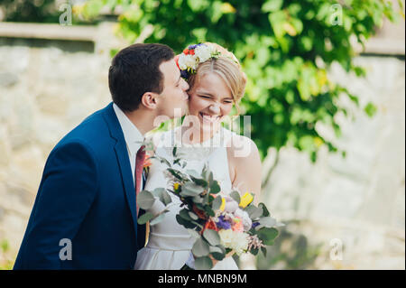Glücklich lächelnde stilvolle Braut und Bräutigam im Sommer, grünen Park mit Blumenstrauß, Tanzen und Spaß am Tag ihrer Hochzeit Stockfoto