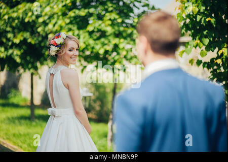 Glücklich lächelnde stilvolle Braut und Bräutigam im Sommer, grünen Park mit Blumenstrauß, Tanzen und Spaß am Tag ihrer Hochzeit Stockfoto