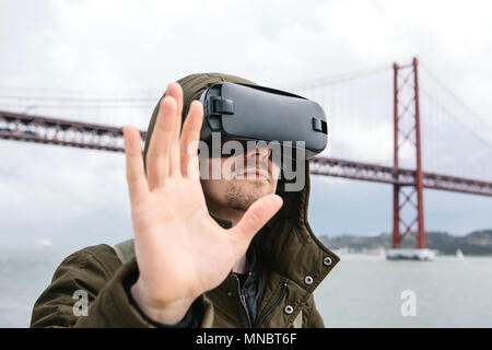 Ein Mann mit Virtual reality Brillen. 25 April Brücke in Lissabon im Hintergrund. Das Konzept der Virtuellen reisen. Das Konzept der modernen Technologien und deren Einsatz im täglichen Leben Stockfoto