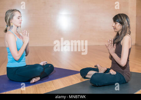 Zwei junge Frau: Eine blonde kaukasischen und eine indische sitzen in einem Lotus Position in einem Yoga Studio. Stockfoto