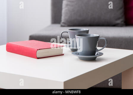 Nahaufnahme einer Couchtisch mit zwei graue Schalen und einem Buch in roten Deckel, neben einem verschwommenen grau Sofa im Hintergrund Stockfoto