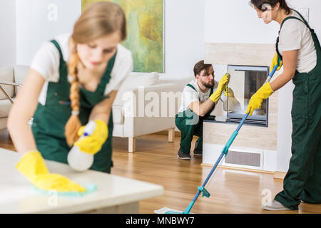 Drei junge professionelle Reinigungskräfte in Uniformen Reinigung geräumiges Wohnzimmer Stockfoto