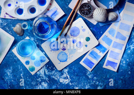 Kreative Künstlerin Arbeitsplatz mit marine Aquarell, Paletten, Muster, Pinsel und Wasser Gläser von oben. Malerei Meer Konzept auf einem marine blau backgroun Stockfoto