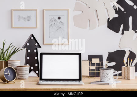 Laptop mit weißer Bildschirm auf einem Schreibtisch aus Holz mit Uhr, Tasse und Bleistifte sowie Wand Dekorationen Stockfoto