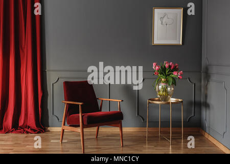 Rot Holz Sessel neben Gold Tisch mit Blumen im Wohnzimmer Interieur mit Poster Stockfoto