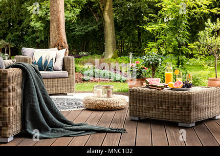 Close-up von Rattan Tisch mit Obst und Saft darauf steht auf einer hölzernen Terrasse in einem Spa Garten Stockfoto