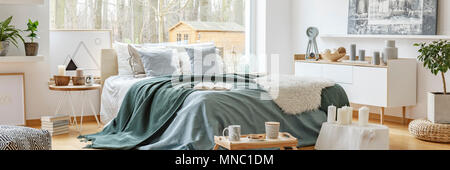 Grüne Decke auf ein gemütliches Doppelbett durch ein großes Fenster im skandinavischen Stil Schlafzimmer Innenraum mit Blick auf einen Wald Stockfoto