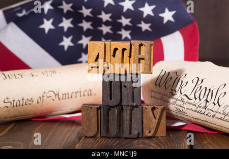 "4. Juli"-Schild mit hölzernen schreiben Bausteine mit den Vereinigten Flaggenstaaten, die Unabhängigkeitserklärung und die Verfassung im Hintergrund - amerikanischen Feiertag Stockfoto