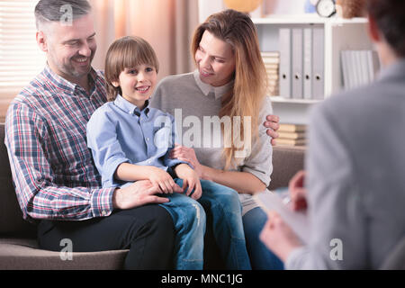 Glückliches Kind sitzt auf dem Schoß seines Vaters neben seiner Mutter während eines Treffens mit dem beratungslehrer Stockfoto