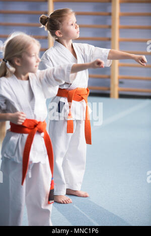 Junge Mädchen tragen orange Gürtel, Ausbildung bewegt sich und suchen in Richtung ihrer Trainer während Karate Klassen Stockfoto