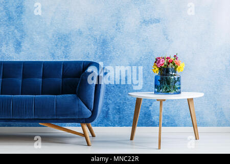 Blumen auf weißem Holz Tisch neben Navy Blue suede Couch in eleganten Wohnzimmer Innenraum Stockfoto