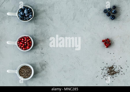 Blick von oben auf eine symmetrische Anordnung von Blaubeeren, Granatapfel und Samen auf einem grauen Tabelle. Stockfoto