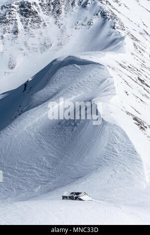 Bergrücken mit großen Wind verpackt Gesimse schiefen über teilweise Schnee alpinen Berghütte abgedeckt Stockfoto