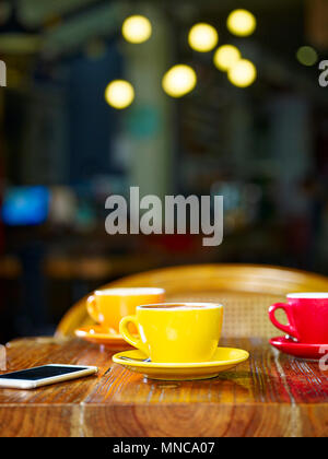 Drei Tassen Cappuccino und ein Handy am Tisch in einem Café Stockfoto