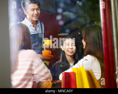 Jungen asiatischen Kellner weiblichen Kunden im Coffeeshop serviert, Schuß durch Fensterglas. Stockfoto