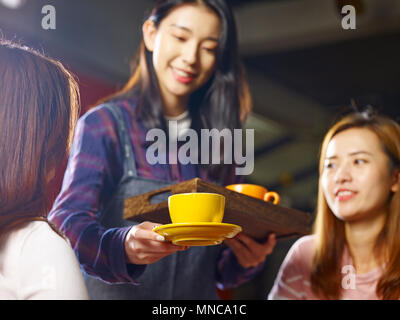 Junge lächelnde asiatische Kellnerin Kaffee zu Kunden, auf den Pokal konzentrieren. Stockfoto