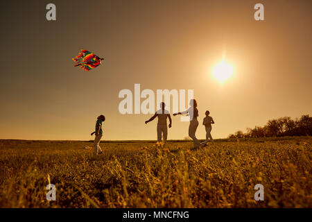 Glückliche Familie mit einem Drachen spielen bei Sonnenuntergang im Feld Stockfoto