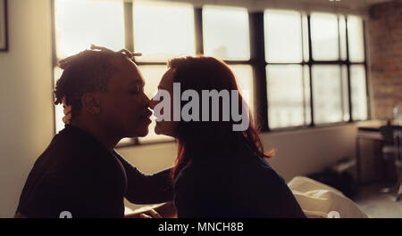 Zärtlich Paar über einander zu küssen im Schlafzimmer. Interracial Mann und Frau sitzt auf dem Bett und Küssen. Stockfoto