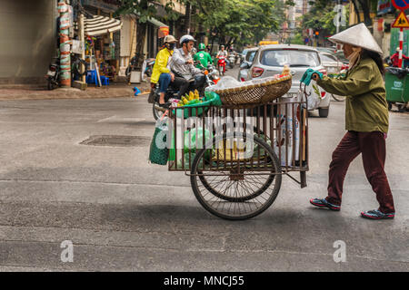 Hanoi, Vietnam - 27. Oktober 2017: Straßenhändler in Hanoi ist schob ihren Warenkorb mit Waren. Altstadt von Hanoi, Vietnam Stockfoto