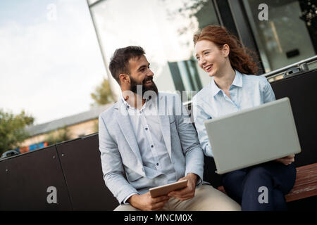 Zwei lächelnde junge Geschäftsleute arbeiten an Tablet im Freien Stockfoto