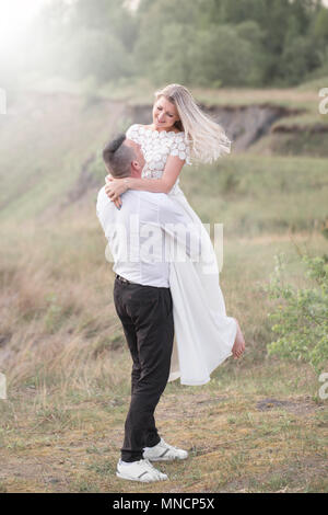 Schöne liebe Leute, Brautpaare, ein junges Paar, outdoor Session. Die Braut in einem weißen Kleid. Liebe, Hochzeit, Leidenschaft. Wirbel, die auf den Händen Stockfoto