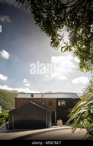 Äußere Aufnahme der ganzen Haus gegen Sonnenschein mit Bäumen in der oberen Ecke. KoroKoro Haus, Wellington, Neuseeland. Architekt: Solari Architekten, 2018. Stockfoto