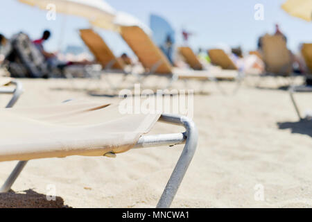 Nahaufnahme von einigen beige liegen und einige beige Sonnenschirme in La Barceloneta Beach, in Barcelona, Spanien, mit unkenntlich Menschen Sonnenbad in der Stockfoto