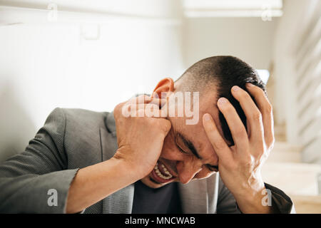 Nahaufnahme eines Leidens kaukasischen Mann mit einer Hand in seinem Kopf und mit der anderen Hand über sein Ohr Stockfoto