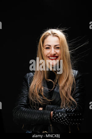 Foto des Blonden lächelnd in Lederjacke mit Waffen an der Taille auf leeren schwarzen Hintergrund gekreuzt Stockfoto