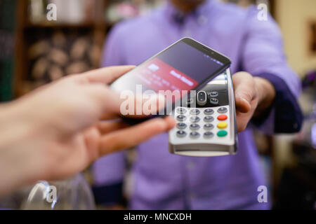 Bild der Käufer zahlt mit Smartphone in der Nähe der Verkäufer Mann mit Terminal in Store Stockfoto