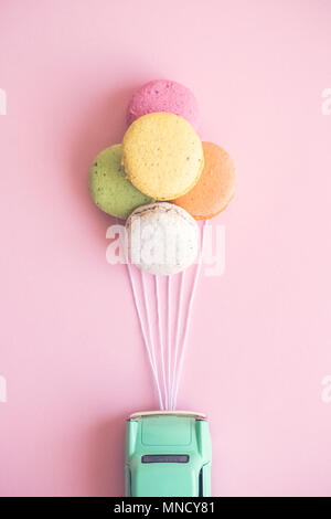 Kleine retro Auto zu bunte Makronen in Form von Helium Ballons auf Pastell rosa Hintergrund minimal kreatives Konzept beigefügt. Stockfoto