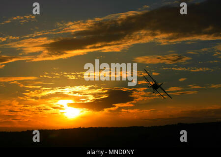 Eine schöne, magneficient Moment, wenn ein doppeldecker fliegen über den Himmel, während die Sonne hinter ihm geht. Stockfoto