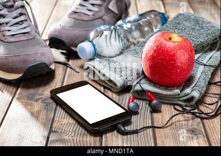 Nahaufnahme von einem roten Apfel, Sportschuhe, audio Kopfhörer, Smartphone, Handtuch und Trinkflasche auf einem antiken Holztisch fotografiert. Stockfoto