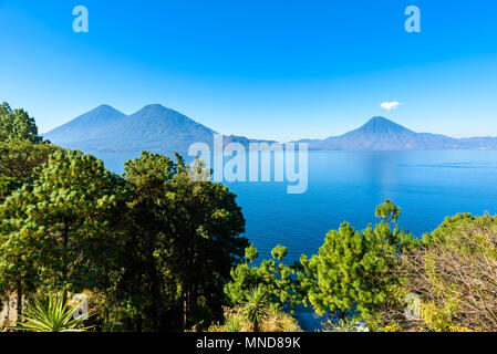 Blick von der Atitlan See am frühen Morgen, blauer Himmel, klares Wasser, wunderschöne magic See mit Vulkanen und indigene Bevölkerung im Hochland von Gu Stockfoto