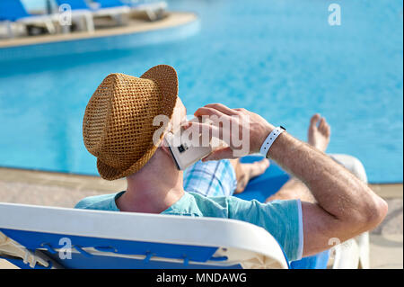 Mann mit Handy im Urlaub am Pool im Hotel, Konzept der Freiberufler arbeiten für sich selbst im Urlaub und Reisen Stockfoto