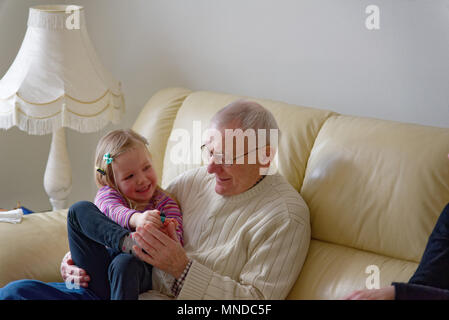 Großvater und seine drei Jahre alte Enkelin zusammen lachen setzte sich auf ein Sofa Stockfoto