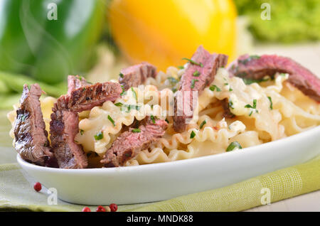 Italienische Tagliatelle mit Streifen von gegrilltes Sirloin, im Hintergrund Salat und rote und grüne Paprika Stockfoto