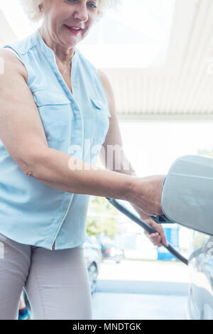 Active Senior lächelnde Frau beim Befüllen des Gastanks von ihrem Auto Stockfoto