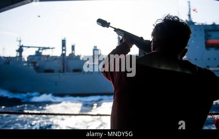 180515-N-OY 799-0095 GEWÄSSER SÜDLICH VON JAPAN (15. Mai 2018) Flieger rekrutieren Micha Spinella, aus Bakersfield, Kalifornien, Brände ein Bote zu militärischen Sealift Command (MSC) Dry Cargo/Munition ship USNS Cesar Chavez (T-AKE 14), aus dem Hangar Bay an Bord der Marine vorwärts - bereitgestellt Flugzeugträger USS Ronald Reagan (CVN 76), als Teil einer Auffüllung-auf-See während der Probefahrt, 15. Mai 2018. Die nicht-Kämpfer, zivil-Crewed Charter Schiff, vom MSC betrieben, Benzin, Essen, Kampfmittel, Ersatzteile, Mail und andere Verbrauchsmaterialien zur Marine Schiffen in der ganzen Welt. Ronald Reagan, das Flaggschiff der Träger Stockfoto