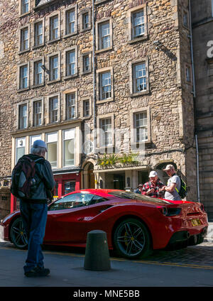 Royal Mile, Edinburgh, 16. Mai 2018. Touristen genießen den Sonnenschein auf der Royal Mile, Edinburgh, Schottland, Vereinigtes Königreich. Leute, die von einem hellen roten Ferrari 488 GTB coupé Sportwagen auf einer doppelten gelben Linie auf dem gepflasterten Royal Mile geparkt neben der St. Giles Cathedral, die neidvolle Blicke Stockfoto