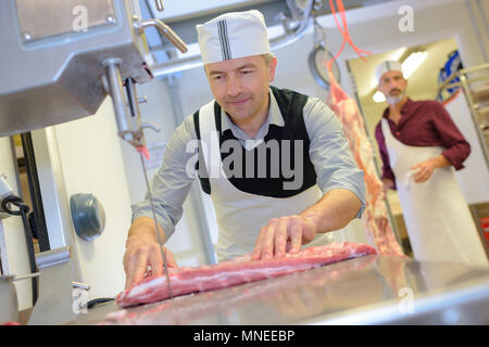 Reife männliche Metzger schneiden von Fleisch auf der Bandsäge Stockfoto
