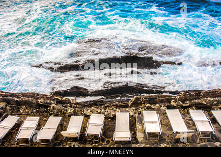 Leeren Strand Stuhl Sonnenliegen Sonnenliegen auf Felsen Felsen stürmischen s Stockfoto